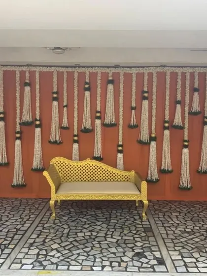 A simple yet elegant backdrop featuring tassels made of fragrant jasmine flowers (mogra). This traditional element is set against a warm orange fabric, perfect for a classic Haldi or Mehndi function.