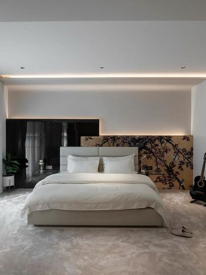 This master bedroom is a study in serene sophistication. A custom laser-cut headboard, plush carpeting, and soft, indirect lighting create a tranquil and inviting atmosphere, with a guitar in the corner adding a personal touch.