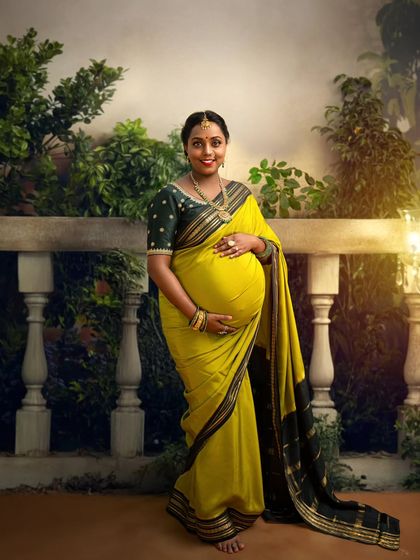 A beautiful solo portrait of a mother-to-be in a vibrant yellow saree, standing on a balcony. The image captures her joyful anticipation and the beauty of traditional attire.
