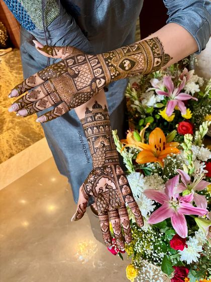 A beautiful shot of a bridal mehendi against a backdrop of fresh flowers. The design features intricate peacock and architectural elements.