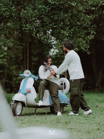 The groom presenting his bride with a bouquet of flowers as she sits on a vintage scooter.