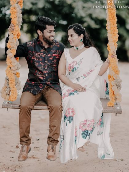 A couple enjoys a moment on a flower-decorated swing, their traditional outfits complementing the rustic, romantic setting.