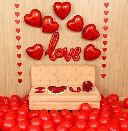 A simple and sweet declaration of love. This setup uses a sea of red balloons on the floor, 'I ❤️ U' spelled out with petals on the couch, and a backdrop of red heart-shaped foil balloons.