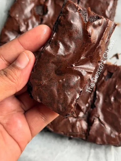 Holding up a piece of my classic brownie to show off its signature crinkly, paper-thin top. This is the result of a perfectly balanced recipe.