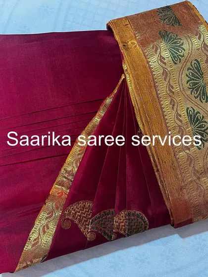 A maroon saree with a unique gold and green border design.