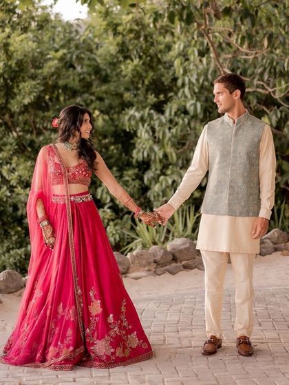 Tailored in togetherness. This shot captures the couple's coordinated Sangeet look, with her in a vibrant pink lehenga and him in a complementary pastel ensemble.