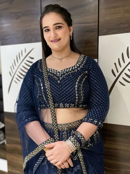 A simple yet elegant look for a party, featuring a subtle smokey eye and a glossy lip. The hair is styled straight and sleek, complementing the modern navy blue lehenga.