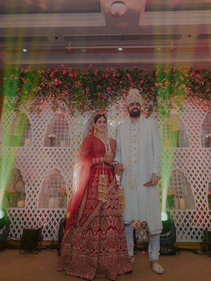 The couple poses for a photo after their Varmala, looking regal against the beautifully lit 'jaali' backdrop.