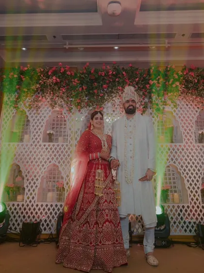 The couple poses for a photo after their Varmala, looking regal against the beautifully lit 'jaali' backdrop.