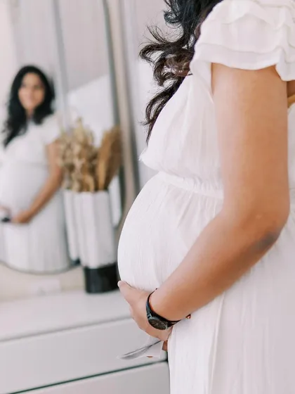 A detail shot focusing on the baby bump, with the mother's reflection in the mirror. This creative composition highlights the physical transformation of pregnancy in an artistic way.