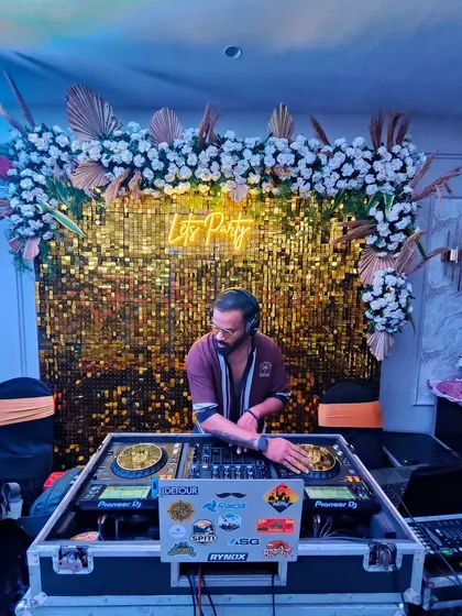Behind the decks at a private party with a beautiful floral and gold sequin backdrop. I can set up my console to blend seamlessly with your event's decor.