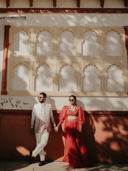 A stylish couple poses against a wall with traditional Indian architectural details. The contrast between the harsh sunlight and shadows adds a modern, graphic quality to this heritage shoot.