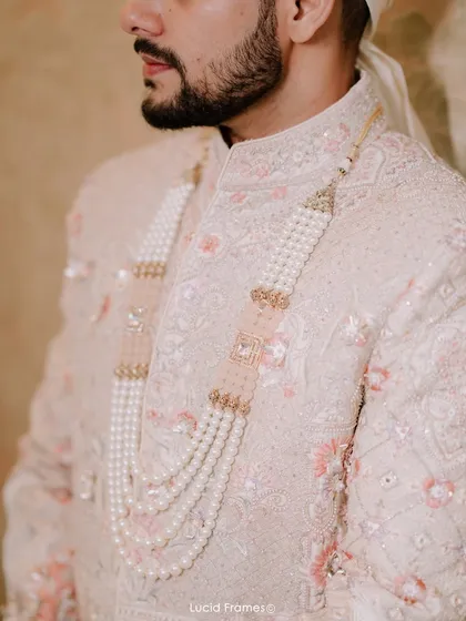 A detail shot of the groom's sherwani and the elegant pearl necklace (satlada), highlighting the richness of his wedding attire.