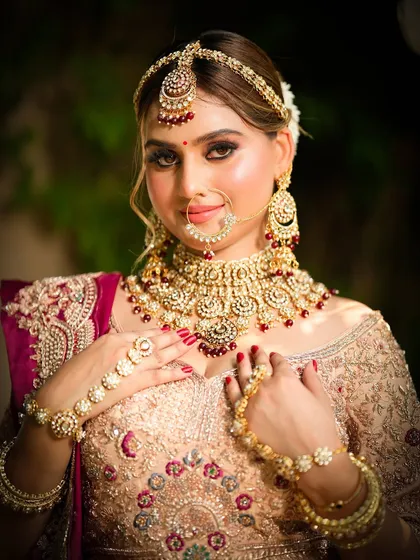 An elegant bridal look featuring a peach and maroon lehenga. The makeup is a soft glam with defined, smokey eyes and a neutral lip, paired with a classic updo.