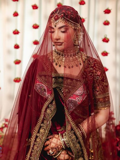 A beautiful shot of the bride under her veil, the rich maroon fabric and intricate gold embroidery creating a look of timeless tradition and grace.