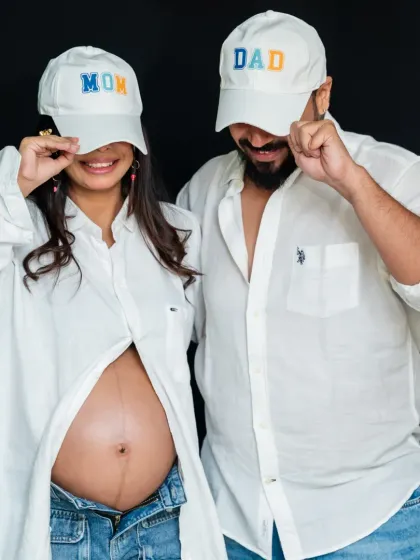 Studio sessions can be fun and modern too. Using simple props like 'Mom' and 'Dad' caps, we created a playful and stylish portrait that shows off the baby bump and the couple's personality against a clean, classic black backdrop.