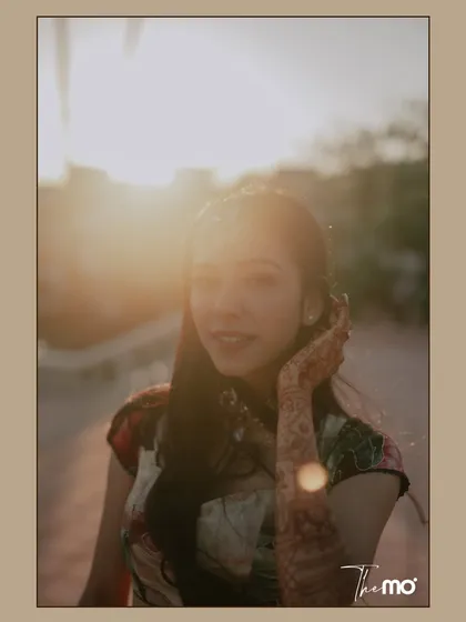 A sun-kissed portrait of the bride during her Mehendi event in Kenya. The golden hour light creates a beautiful flare, highlighting her joyful expression and the intricate henna on her hand.