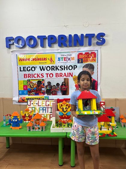 At our Footprints center, a student shows her completed LEGO pandal in front of a table showcasing the workshop's creations.