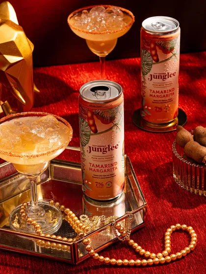 A rich, luxurious shot of the Tamarind Margarita. The deep red background, gold accents, and pearl necklace create a feeling of opulence and indulgence.