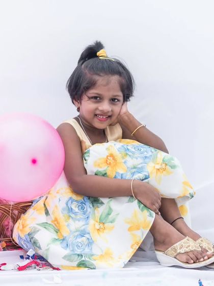A portrait of pure joy. This little one is surrounded by pink balloons, wearing a beautiful floral dress that perfectly complements her happy spirit.