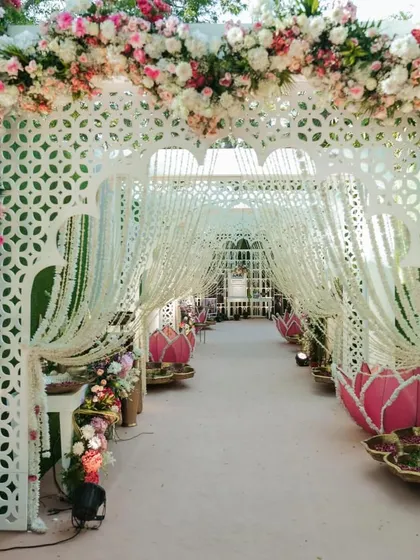 A beautiful entrance walkway for the Lotus Mandap wedding. The path is lined with illuminated lotus installations and features a series of white jaali arches draped with hanging florals.