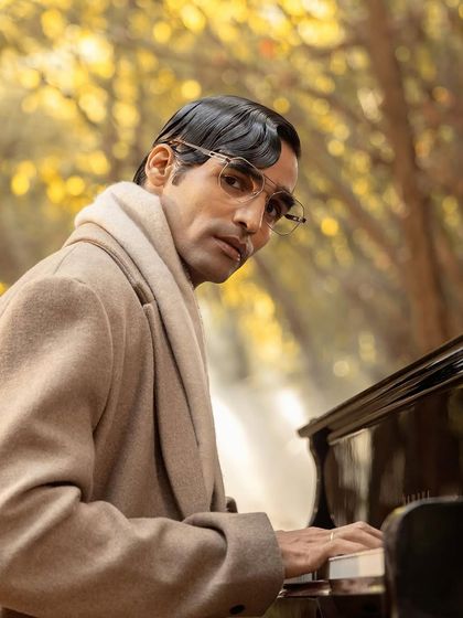 A profile shot for John Jacobs, capturing the model at the piano in a classic winter coat, creating a narrative for the eyewear campaign.