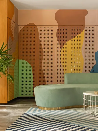 The waiting area features a stunning feature wall with perforated panels painted in an abstract, organic pattern of earthy colors. The curved green sofa and striped rug create a comfortable and visually stimulating environment for families.