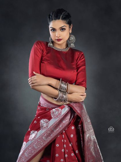 A close-up portrait in a red fusion saree look, highlighting the model's expression and the silver jewelry. The dark studio background makes the red top and silver accessories stand out.