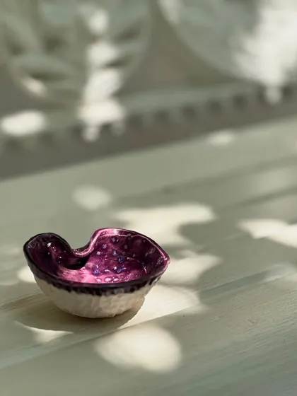 A tiny, organic-shaped pinch pot with a brilliant purple interior that sparkles in the light. This piece embodies the spirit of the Kaleidoscope Collection, where even the smallest ceramic can make a big statement.