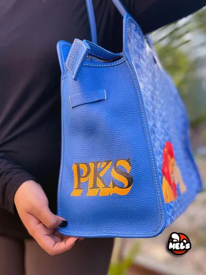A side view of the Goyard tote, featuring the client's personalized initials "PKS" painted in a bold, 3D style.