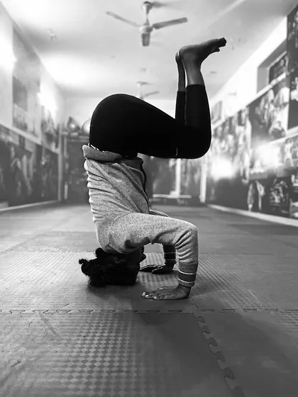 A student practices a headstand, a gymnastics exercise that builds shoulder stability, core strength, and balance.