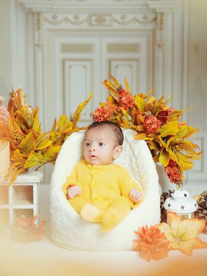 This newborn is sitting comfortably in a soft chair, surrounded by warm autumn colors. I have a variety of props to match any season or theme.