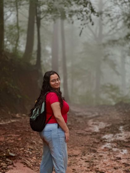 A trekker looks back with a smile while walking on a misty, muddy trail in Gangadikal.