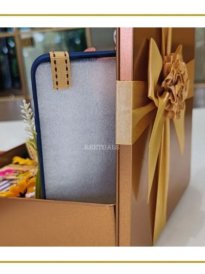 This gift is presented in a unique box with a ribbon-tie closure. The warm, earthy tones of the box and the handmade paper flower on the bow give it a sophisticated and artisanal feel.