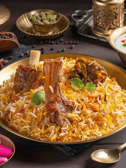 Mutton Biryani styled in a traditional brass plate. The shot highlights the tender, fall-off-the-bone meat and fragrant rice, making it a centerpiece for The Mughal House's menu.