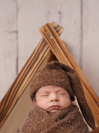 A slightly different angle of the camping-themed newborn portrait, with the wooden tent frame creating a lovely visual element. The focus remains on the baby's serene and sleepy face.