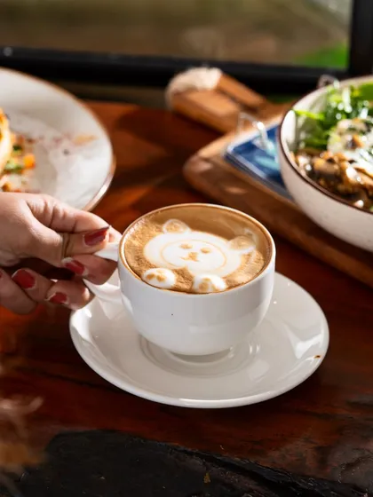 A cute bear latte art being held by a customer. This shot highlights a unique, Instagrammable detail that makes a cafe special.