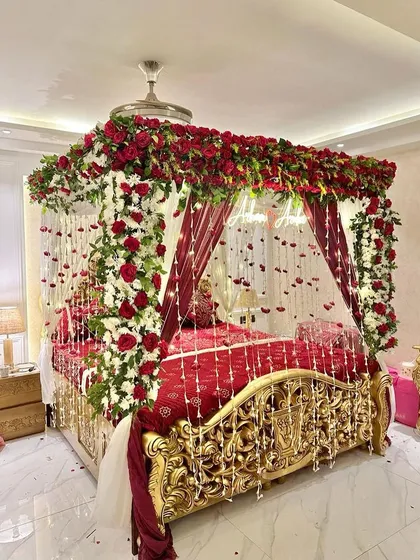 I specialize in working with any room to create a royal experience. This setup features a stunning four-poster bed draped in red and white florals, with hanging flower strings and a custom neon sign, turning the room into a palace.
