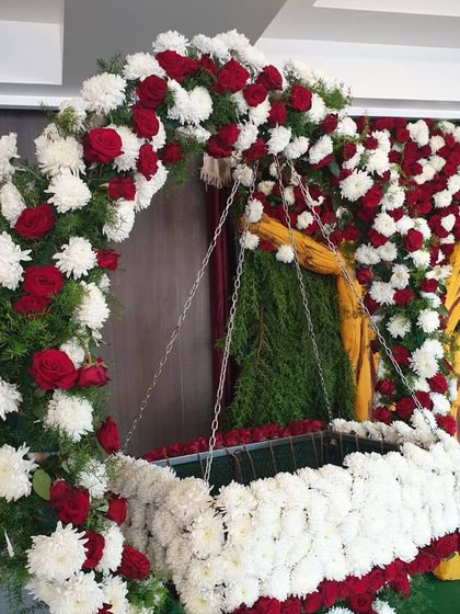 A cradle fully decorated with white chrysanthemums and red roses, part of a larger floral naming ceremony setup.