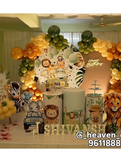 A complete jungle party setup for a first birthday, showcasing a variety of animal cutouts like a tiger, elephant, and giraffe. The decor includes a custom backdrop, themed plinths, and a balloon arch in orange and green.