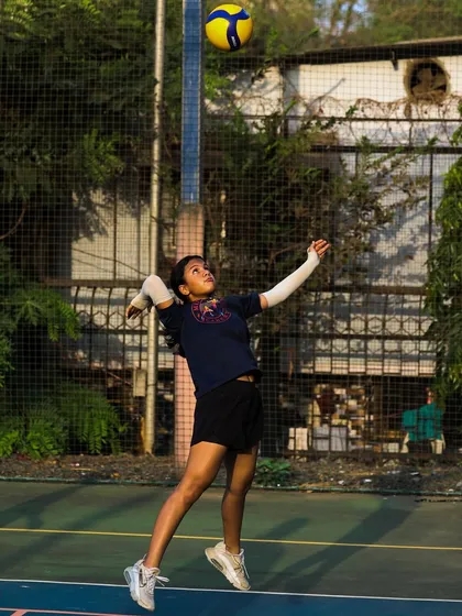 A U-14 player reaches up to serve, demonstrating the technique she has learned in our program.