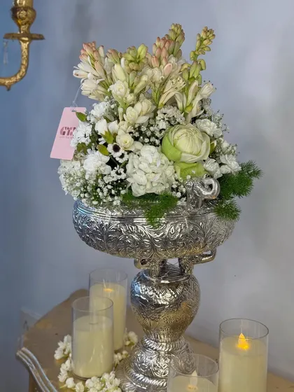 A beautiful festive arrangement featuring an antique silver urli stand filled with fragrant white tuberoses and other blooms, surrounded by glowing candles.