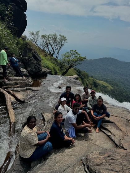 A small group from our Bandaje trek taking a break on the rocks, with the waterfall and lush green valley in the background.