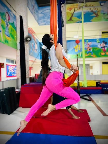 A student demonstrates a beautiful lunge pose mid-air, showcasing her flexibility and balance on the orange aerial silks.