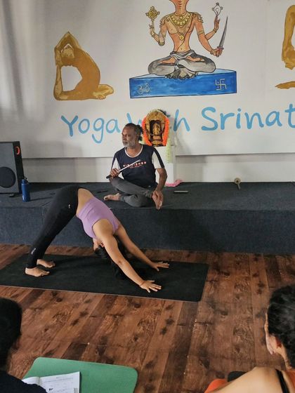 A student demonstrates a well-aligned Downward-Facing Dog as a teacher plays the flute, creating a serene and focused atmosphere.