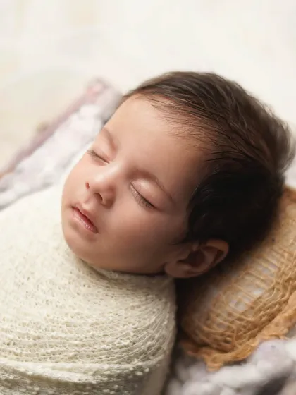 A detailed portrait of the sleeping newborn's face, resting on a tiny burlap pillow. The focus is on his peaceful expression and delicate features.
