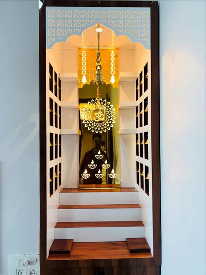 A close-up of a custom-built home mandir, showcasing intricate details. This design incorporates backlit panels with sacred symbols, small niches for idols, and a hanging brass bell, creating a serene and divine corner in your home.