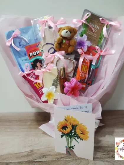 A pink-themed gift bouquet filled with skincare items, a protein bar, a teddy bear, and other small presents, beautifully arranged and wrapped.