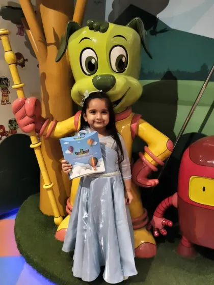 A birthday princess posing proudly with her book next to our mascot, Tinga Dojo.