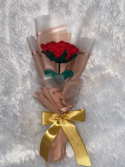 A flat lay of the single red rose bouquet against a soft white background, highlighting its delicate wrapping and rich color.
